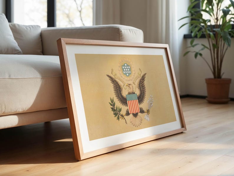 K&ouml;nnte beinhalten: Gerahmter Druck des Gro&szlig;en Siegels der Vereinigten Staaten, mit einem Adler mit ausgebreiteten Fl&uuml;geln, Olivenzweig und Pfeilen. Das Kunstwerk wird in einem hellen Holzrahmen pr&auml;sentiert, der an einem beigen Sofa auf einem Parkettboden lehnt.
