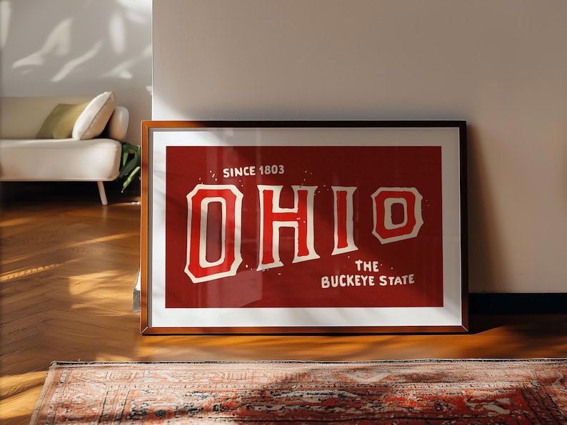 K&ouml;nnte beinhalten: Ein gerahmter Druck mit rotem Hintergrund und wei&szlig;em Text, der "SINCE 1803 OHIO THE BUCKEYE STATE" lautet.
