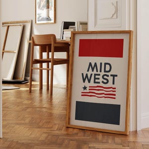 May include: A framed print with a red, white, and blue design. The print features the text "MID WEST" and a stylized American flag. The frame is made of wood and has a natural finish.