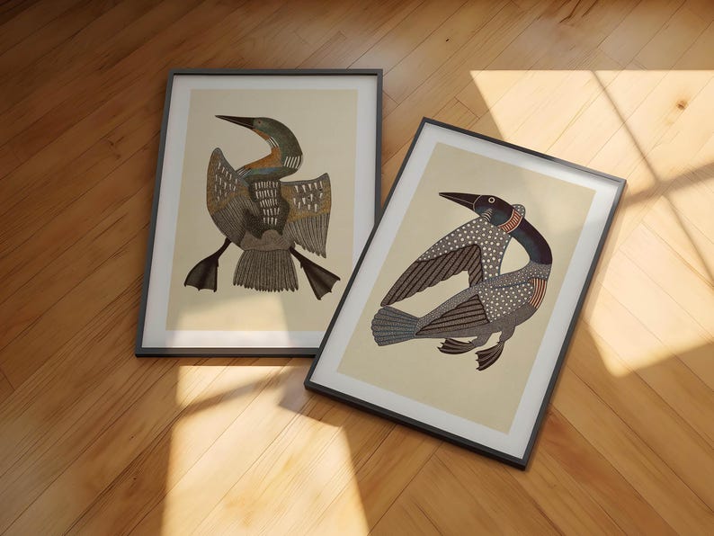 May include: Two framed art prints featuring stylized illustrations of loons. Each print displays a bird with intricate patterns on its wings and body, set against a light cream background. The frames are thin and black, showcasing the detailed avian artwork.