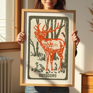Op de afbeelding: Een ingelijste print met een vintage illustratie van een edelhert dat in een bos staat. De print heeft een groene achtergrond en de tekst "OUTDOORS" onderaan.