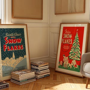 May include: Two framed vintage Christmas posters with the text "Santa Claus 1913 Snowflakes" and "Mica Snowflakes" on a light wood floor. The poster on the left features a snowy mountain scene with a town in the distance. The poster on the right features a red background with a green Christmas tree decorated with ornaments and a star on top.