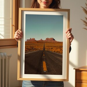May include: A framed photograph of a long, straight road leading to a mountain range in the distance. The road is paved and has a yellow dividing line. The mountains are red and brown and are silhouetted against a blue sky.