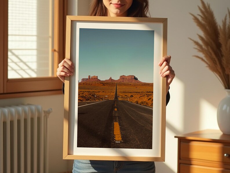 May include: A framed photograph of a long, straight road leading to a mountain range in the distance. The road is paved and has a yellow dividing line. The mountains are red and brown and are silhouetted against a blue sky.