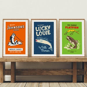 May include: Three framed vintage fishing art prints. The prints feature colorful designs with text including "Johnson's Spoon", "Lucky Louie", and "The Famous Flatfish". The prints are displayed on a rustic wooden bench.