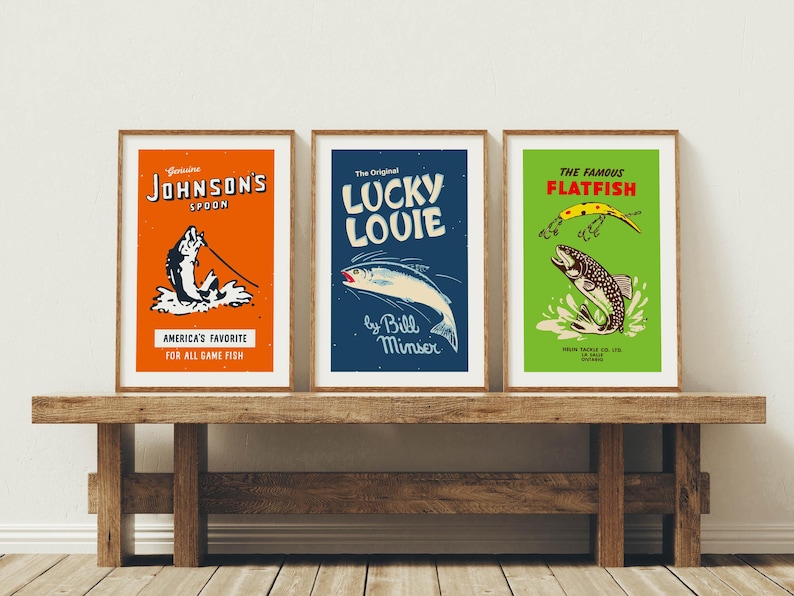 May include: Three framed vintage fishing art prints. The prints feature colorful designs with text including "Johnson's Spoon", "Lucky Louie", and "The Famous Flatfish". The prints are displayed on a rustic wooden bench.