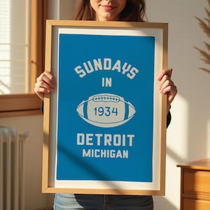 Peut inclure: Une affiche encadr&eacute;e avec un fond bleu et du texte blanc qui dit "Sundays in 1934 Detroit Michigan". Un contour blanc d'un ballon de football est au centre de l'affiche.