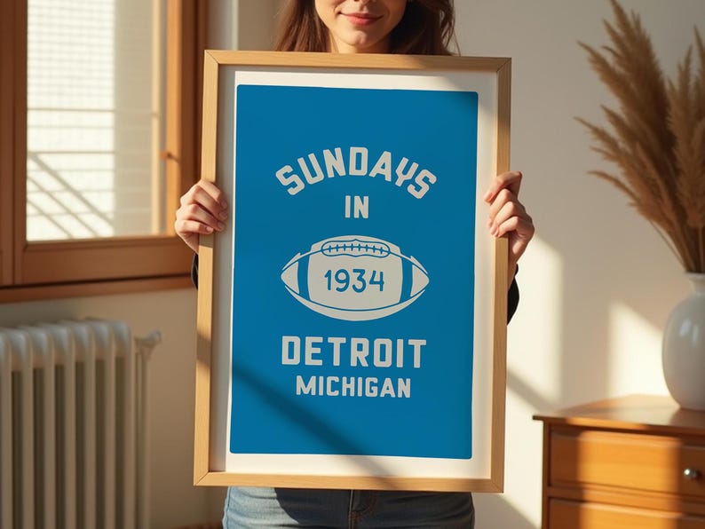 Peut inclure: Une affiche encadr&eacute;e avec un fond bleu et du texte blanc qui dit "Sundays in 1934 Detroit Michigan". Un contour blanc d'un ballon de football est au centre de l'affiche.