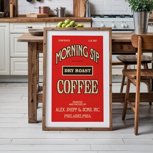 May include: A framed vintage-style coffee advertisement with a red background and cream-coloured text. The text reads "MORNING SIP DRY ROAST COFFEE" and includes the weight as 0.45 kg net. The frame is made of wood. The image is displayed in a kitchen setting.
