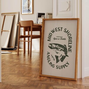 May include: A framed print with a black and white illustration of a fish. The text on the print reads "Mid West Shoreline Angling Supply Superior Quality Gear & Tackle 1976".