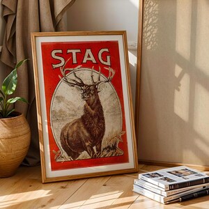 May include: A vintage-style poster with a red background and the word "STAG" in white lettering. A large, detailed illustration of a stag with antlers is featured in the center of the poster.