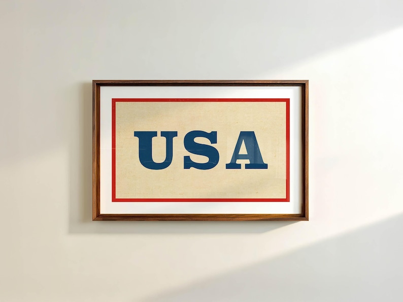 Puede incluir: Impresi&oacute;n enmarcada con la palabra "USA" en letras azules oscuras sobre un fondo crema, bordeada por un marco rojo. La impresi&oacute;n est&aacute; dentro de un marco de madera marr&oacute;n oscuro.