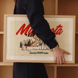 May include: A framed print with a vintage illustration of a canoe on a lake with the text "Minnesota Land of 10,000 Lakes" in red and black lettering.