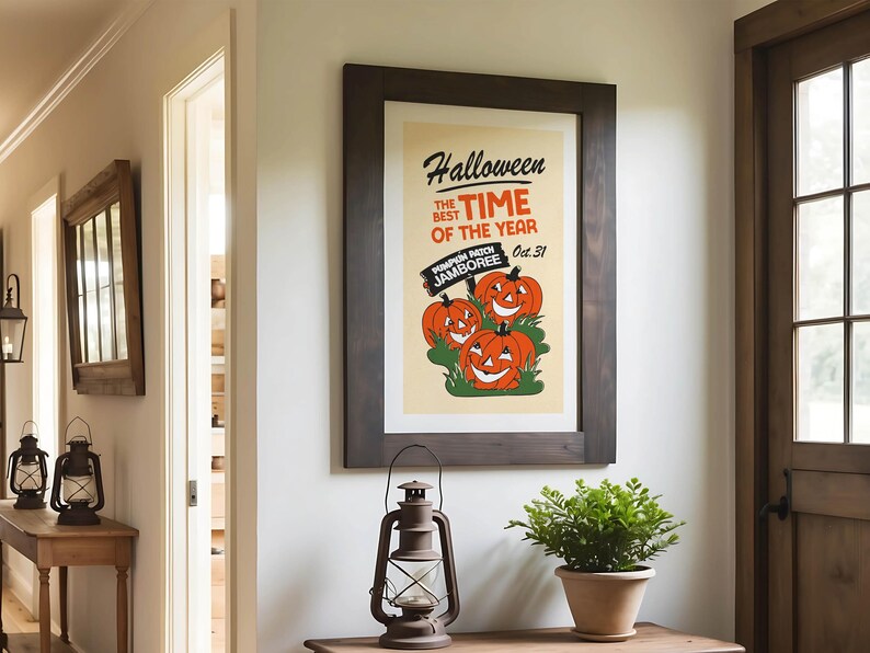 May include: A framed Halloween-themed poster with a dark wood frame. The poster features three smiling orange pumpkins and the text "Halloween, the best time of the year." A vintage lantern and potted plant are on a wooden table.