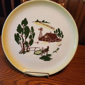 May include: A vintage yellow and white ceramic dinner plate with a brown farmhouse scene. The scene includes a red barn, a windmill, a horse-drawn wagon, and green trees.