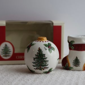 Op de afbeelding: Een set van twee keramische kerstzout- en peperstrooiers. De zoutstrooier is gevormd als een kerstbal en de peperstrooier als een sok. Beide strooiers hebben een groen kerstboomontwerp met rode en gouden accenten.
