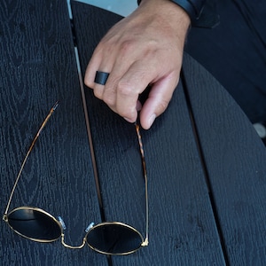 May include: A pair of round, black sunglasses with gold frames and tortoise shell arms. The sunglasses are lying on a black wooden surface.