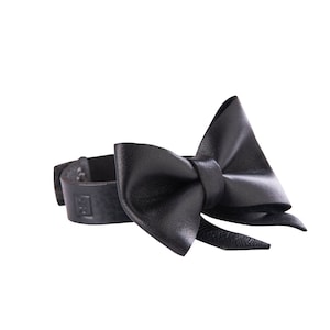 Puede incluir: Una pajarita de cuero negro con una correa para sujetarla a un collar.