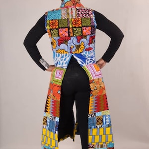 Puede incluir: Un chaleco largo y colorido con un dise&ntilde;o de patchwork. El chaleco tiene un cuello en V profundo y un dobladillo largo y fluido. El chaleco est&aacute; hecho de una variedad de telas, incluyendo algod&oacute;n y seda. El chaleco se lleva sobre una camisa negra de manga larga y pantalones negros. La persona lleva un sombrero blanco de ala ancha.