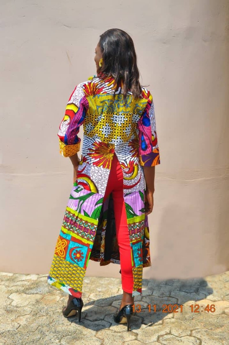 May include: A long, colourful, patterned duster with a split back. The duster is made of a patchwork of different fabrics with a variety of colours and patterns. The person is wearing red trousers and black heels.