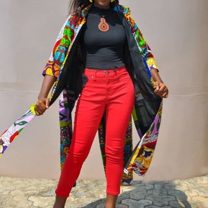 May include: A woman wearing a colourful patterned kimono over a black mock neck shirt and red jeans. She is wearing black high heels and has a brown pendant necklace.