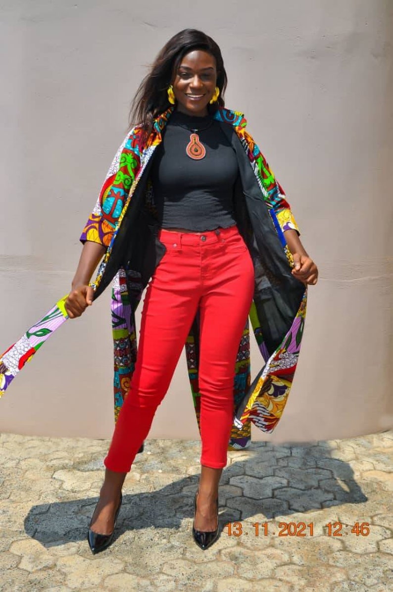 May include: A woman wearing a colourful patterned kimono over a black mock neck shirt and red jeans. She is wearing black high heels and has a brown pendant necklace.