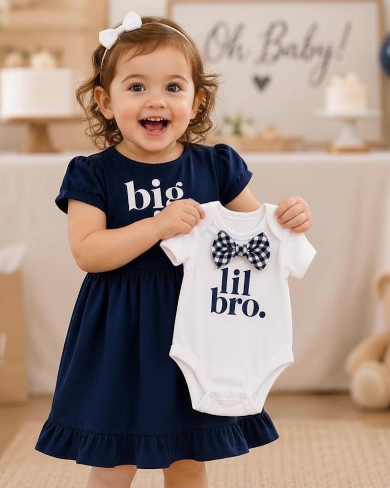 May include: A navy blue dress with short sleeves and the text big printed in white, paired with a white short-sleeved bodysuit featuring the text lil bro. in navy blue and a black and white checkered bow tie attached at the neckline.
