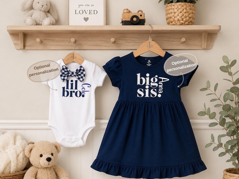 May include: A white short-sleeved bodysuit with a navy and white gingham bow tie and the text "lil bro" in navy blue, paired with a navy blue short-sleeved dress featuring a ruffled hem and the white text "big sis" printed on the front.