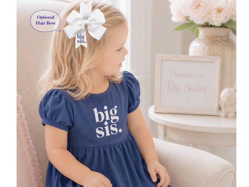 May include: A navy blue dress with short puff sleeves and the white text big sis. printed on the chest. A white hair bow with the text big sis. is attached to the hair. The bow is labeled as an optional hair bow in the image text.