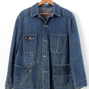 K&ouml;nnte beinhalten: Eine vintage blaue Jeans-Arbeitsjacke mit mehreren Taschen und Knopfverschl&uuml;ssen.