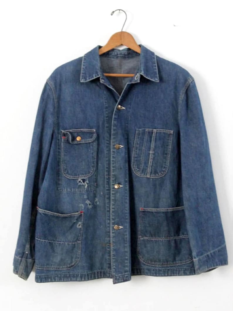 K&ouml;nnte beinhalten: Eine vintage blaue Jeans-Arbeitsjacke mit mehreren Taschen und Knopfverschl&uuml;ssen.