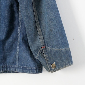 K&ouml;nnte beinhalten: Eine blaue Jeansjacke mit einem roten Stichdetail am &Auml;rmel. Die Jacke hat einen Knopfverschluss und einen einzigen Knopf am &Auml;rmel.