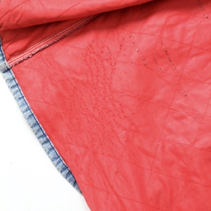 K&ouml;nnte beinhalten: Nahaufnahme des roten gesteppten Futters einer Jeansjacke. Das Futter ist leuchtend rot und hat ein Rautenmuster.
