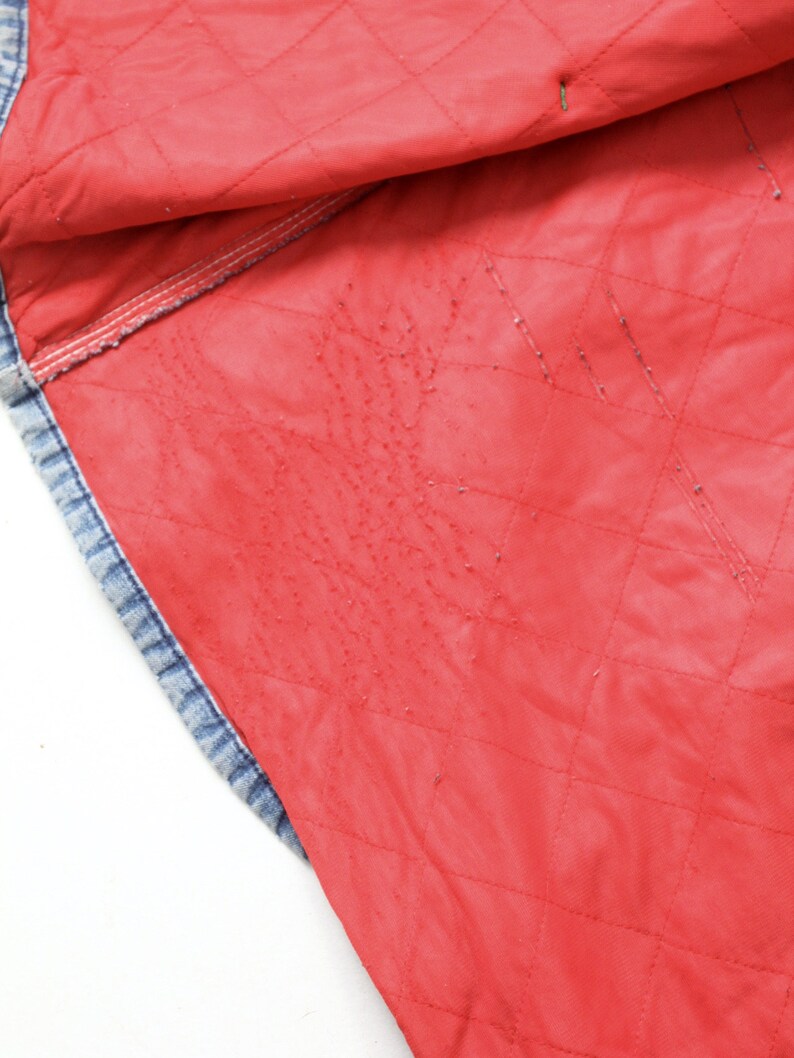 K&ouml;nnte beinhalten: Nahaufnahme des roten gesteppten Futters einer Jeansjacke. Das Futter ist leuchtend rot und hat ein Rautenmuster.
