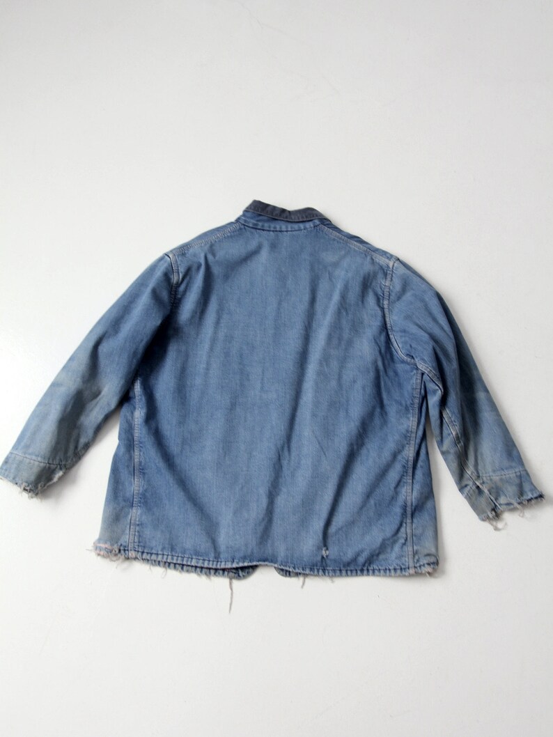 K&ouml;nnte beinhalten: Eine blaue Jeansjacke mit dunkelblauem Kragen. Die Jacke hat einen ausgefransten Saum und &Auml;rmelb&uuml;ndchen.