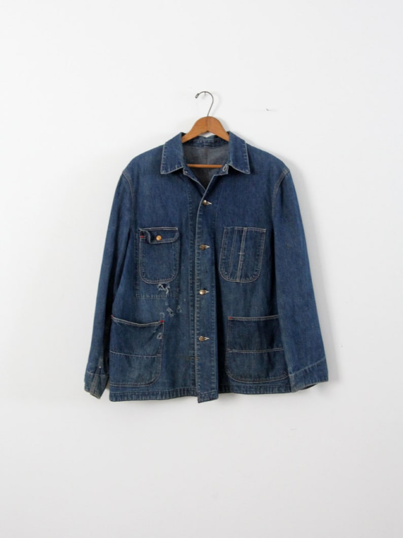 K&ouml;nnte beinhalten: Eine vintage blaue Jeans-Arbeitsjacke mit mehreren Taschen und Knopfverschl&uuml;ssen.
