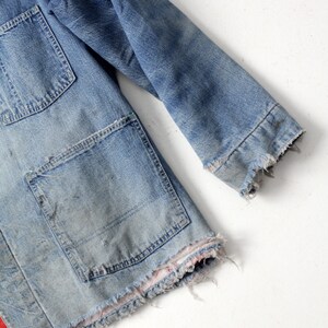 K&ouml;nnte beinhalten: Eine Vintage-Jeansjacke mit ausgefransten Kanten und einer aufgesetzten Tasche. Die Jacke ist hellblau und hat einen abgenutzten Look.