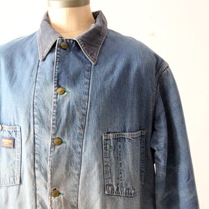 K&ouml;nnte beinhalten: Eine blaue Jeans-Arbeitsjacke mit einem Cordkragen. Die Jacke hat mehrere Taschen und einen ausgewaschenen Look.