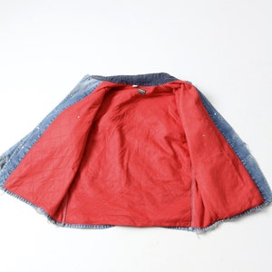 K&ouml;nnte beinhalten: Eine blaue Jeansjacke mit rotem gestepptem Futter. Die Jacke ist ge&ouml;ffnet und auf links gedreht, so dass das Futter sichtbar ist.