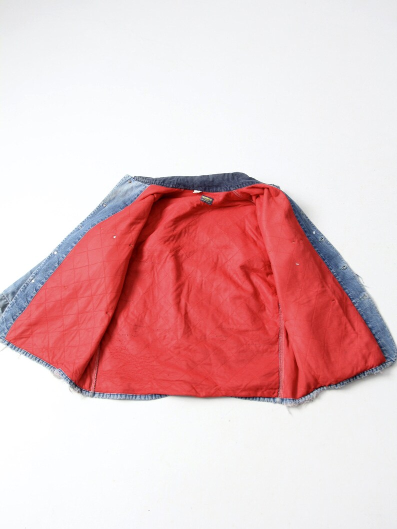 K&ouml;nnte beinhalten: Eine blaue Jeansjacke mit rotem gestepptem Futter. Die Jacke ist ge&ouml;ffnet und auf links gedreht, so dass das Futter sichtbar ist.
