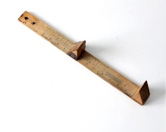 May include: Vintage wooden ruler with a sliding triangular piece. The ruler is marked with inch measurements and has a dark brown color. The ruler is angled across a white background.