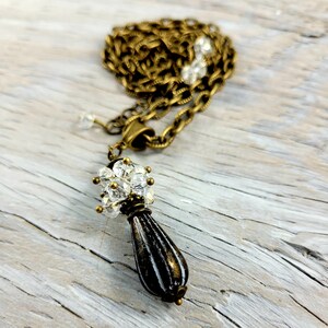 May include: A gold chain necklace with a black and white teardrop pendant. The pendant is topped with a cluster of clear crystals.