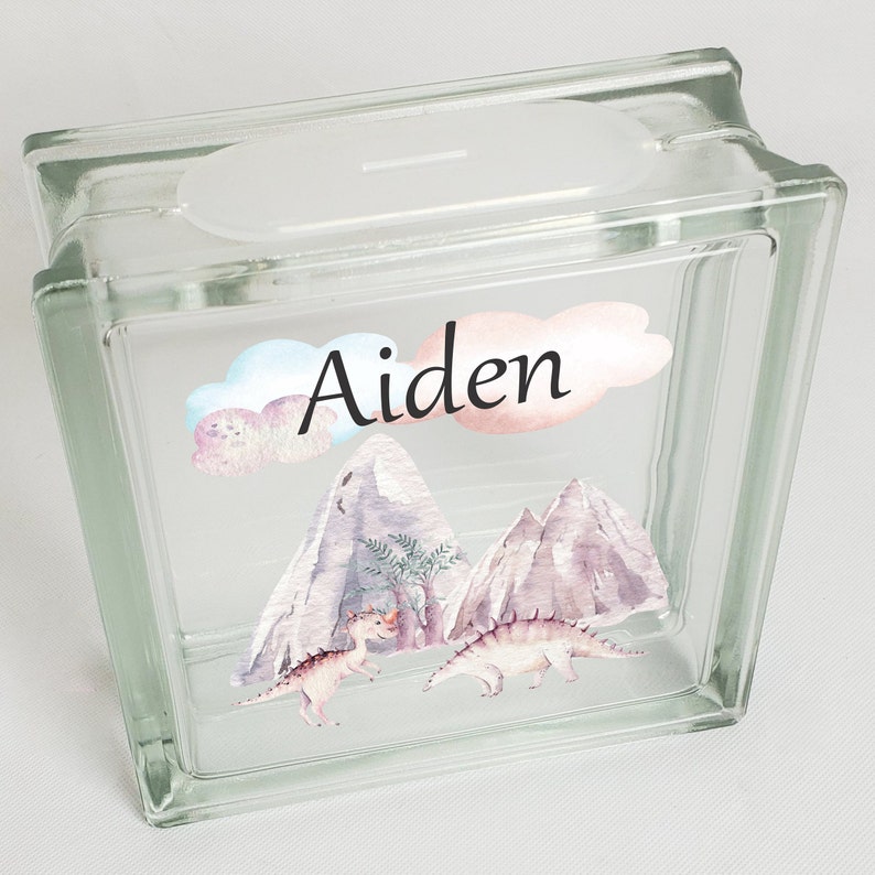 Puede incluir: Huchas de vidrio con un dise&ntilde;o de acuarela de monta&ntilde;as, dinosaurios y nubes. El nombre "Aiden" est&aacute; escrito en la parte delantera.