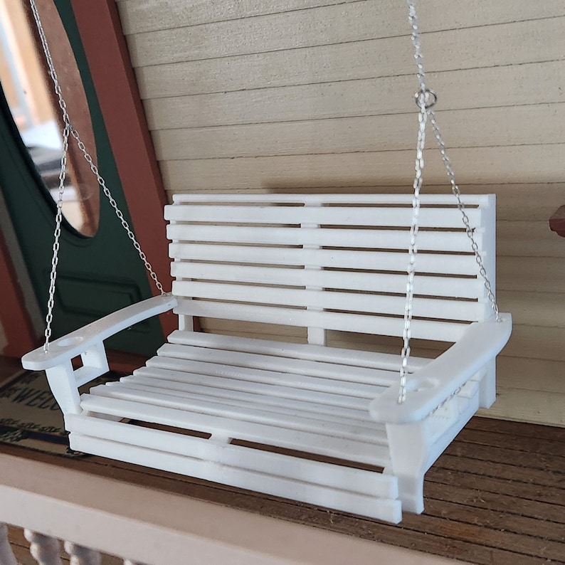May include: White wooden porch swing with a slatted back and seat. The swing is hanging from two silver chains.
