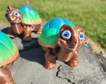 May include: Three small, hand-painted turtle figurines with green and blue shells and brown bodies. The turtles have large, expressive eyes and friendly smiles.