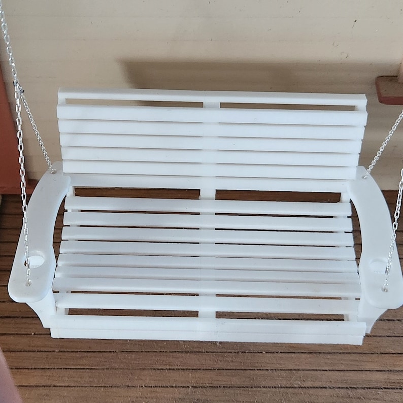 May include: White wooden porch swing with slatted back and curved armrests. The swing is hanging from two chains.