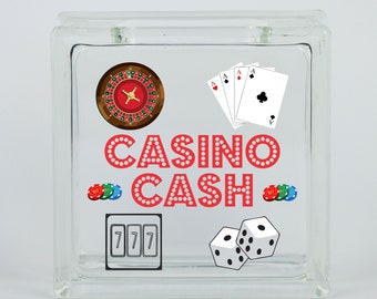 May include: A glass block money jar with a casino theme. The jar has a red and white "CASINO CASH" design with images of a roulette wheel, playing cards, dice, and a slot machine.