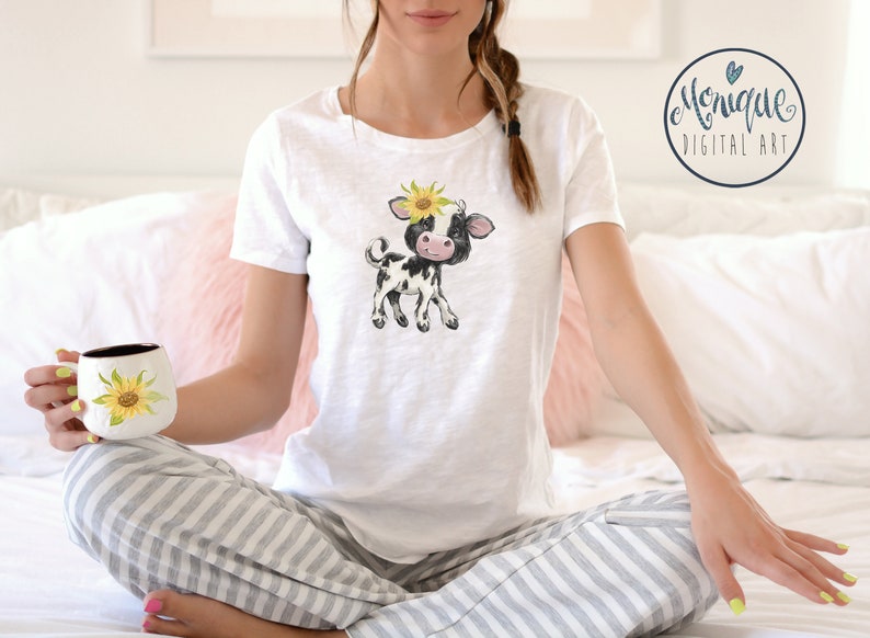 May include: A white t-shirt with a black and white cartoon cow wearing a sunflower on its head. The cow is standing on all four legs and has a pink nose.