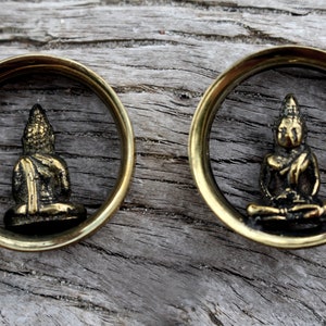 May include: A pair of brass ear gauges with a small golden Buddha statue inside each gauge.