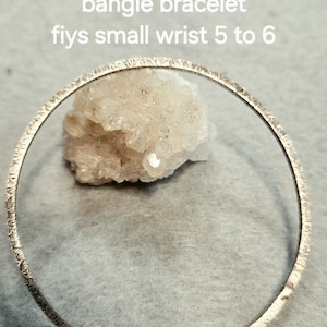 May include: A .925 sterling silver square wire bangle bracelet with a textured surface. The text on the image reads: .925 square wire bangle bracelet fiys small wrist 5 to 6. The bracelet is circular and metallic in appearance.